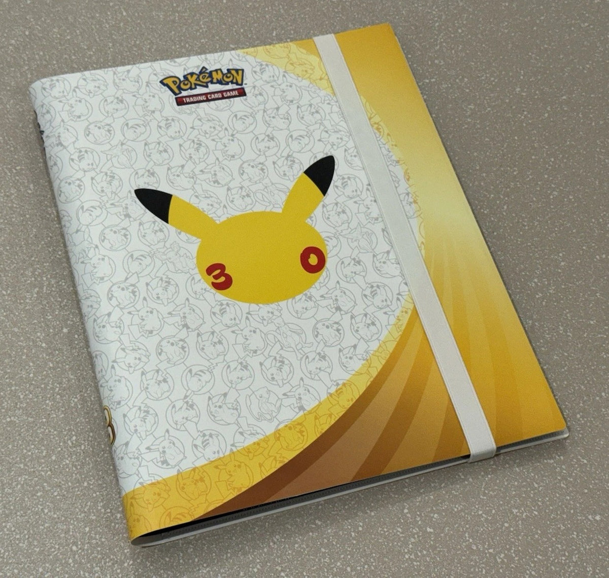 30th Celebration Pikachu binder at an angle showing its spine, depth and white elastic strap