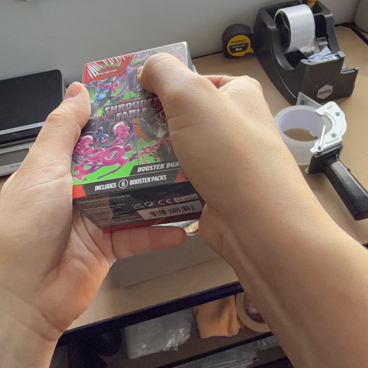 A sealed Pokemon TCG booster bundle being hand-checked over the packing bench before it is packed