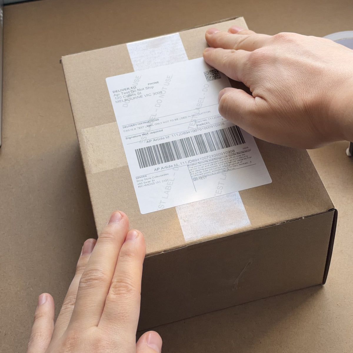 A shipping label being smoothed onto a taped Drop Store parcel
