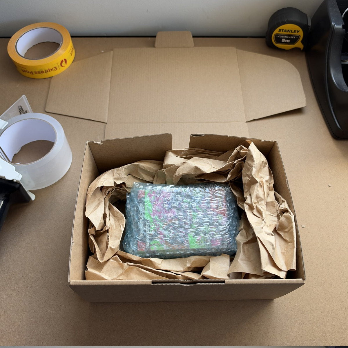 Overhead view of a Drop Store order part-packed: product wrapped in a box with paper void fill, tape gun alongside