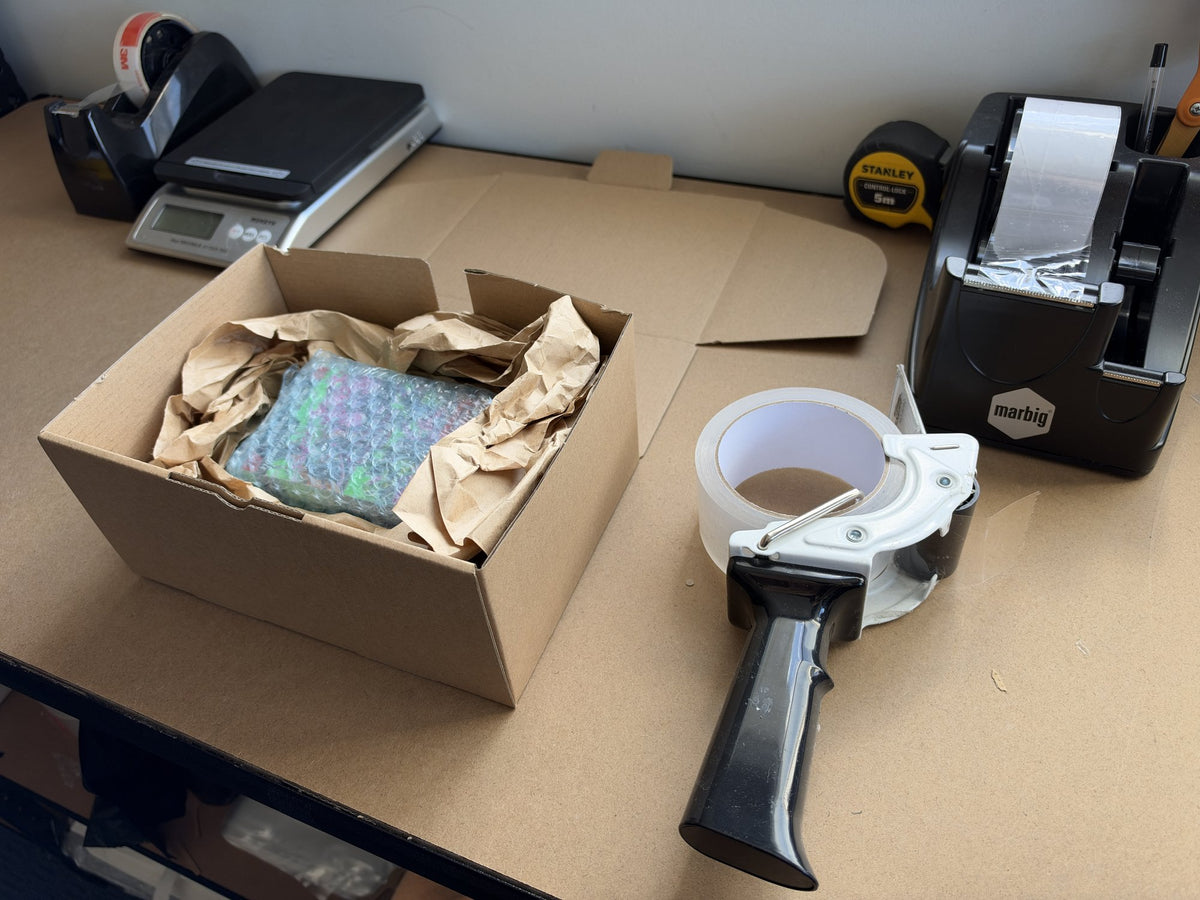 Drop Store packing bench in Melbourne: an order boxed with paper void fill beside the tape gun, scales and label printer